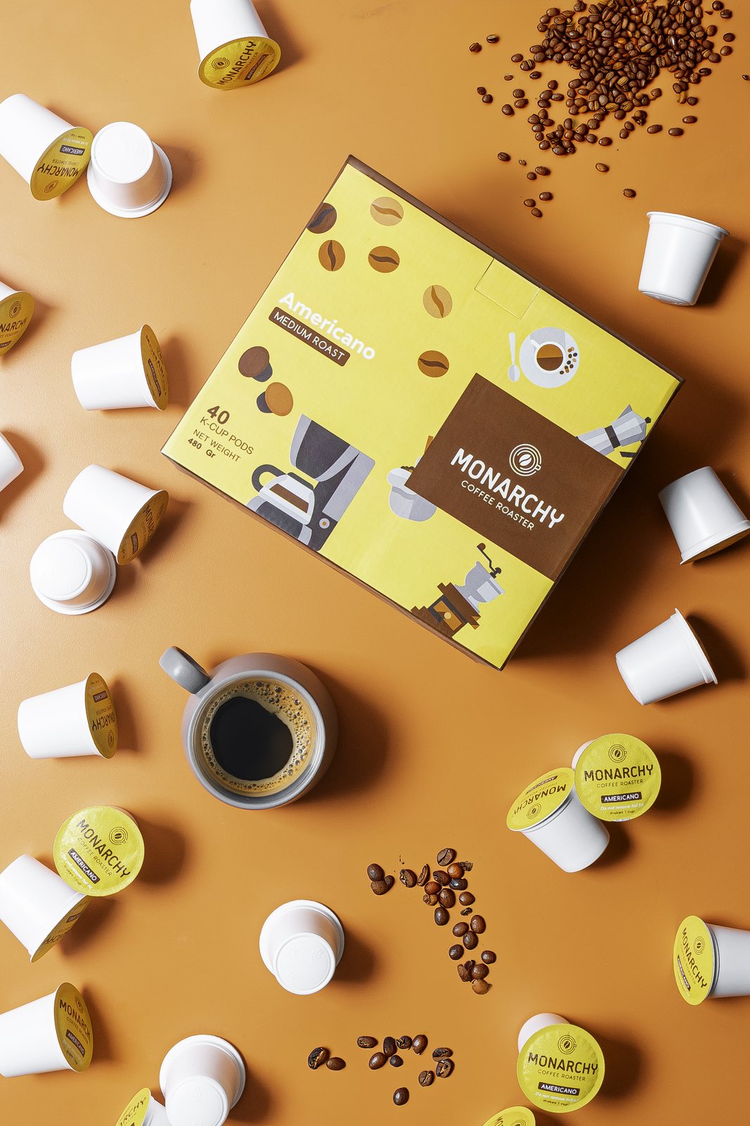 Boks kopi kapsul Monarchy dengan biji kopi dan cangkir kopi