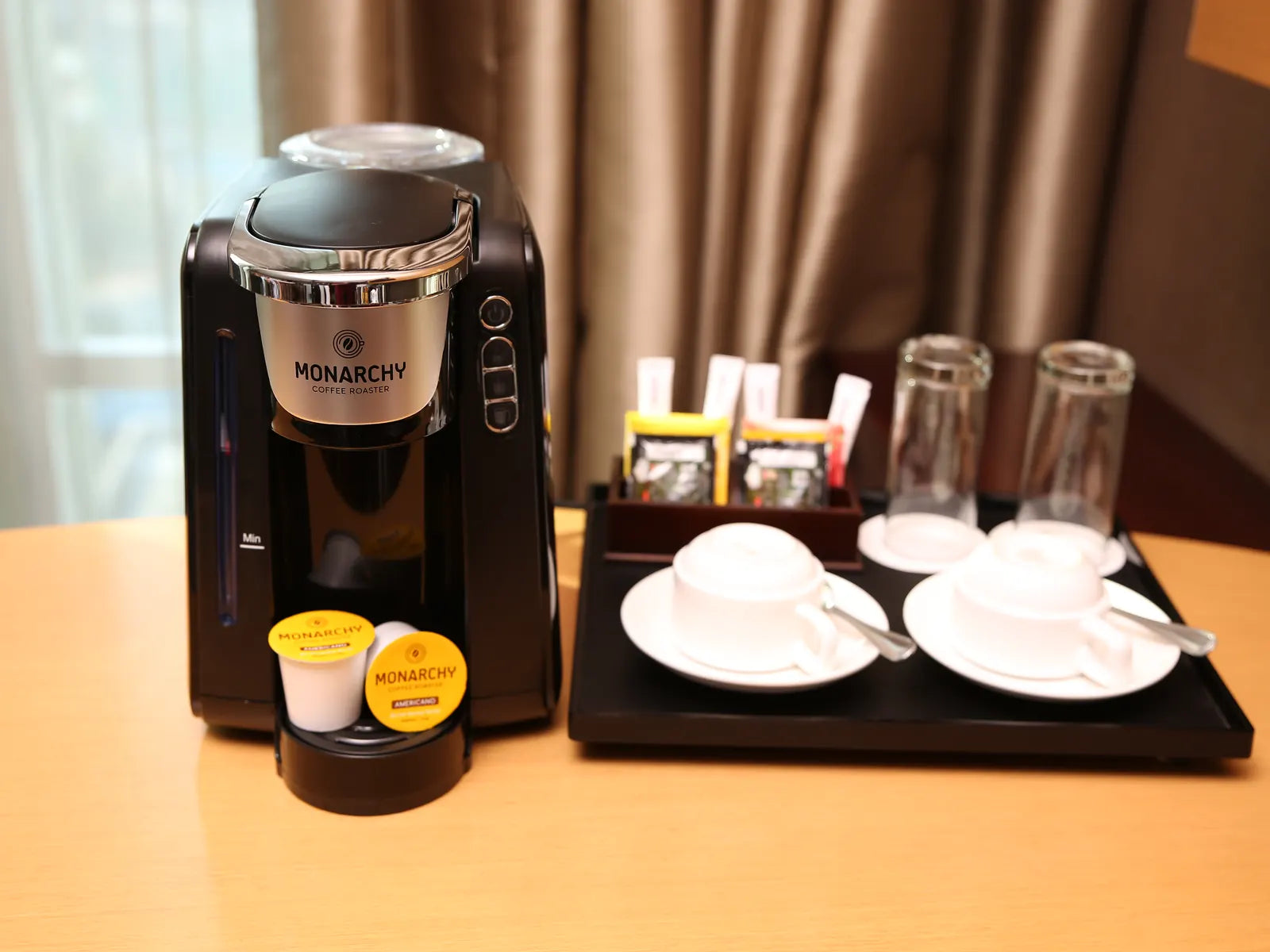 Mesin kopi kapsul Monarchy dan set kopi di meja kamar hotel